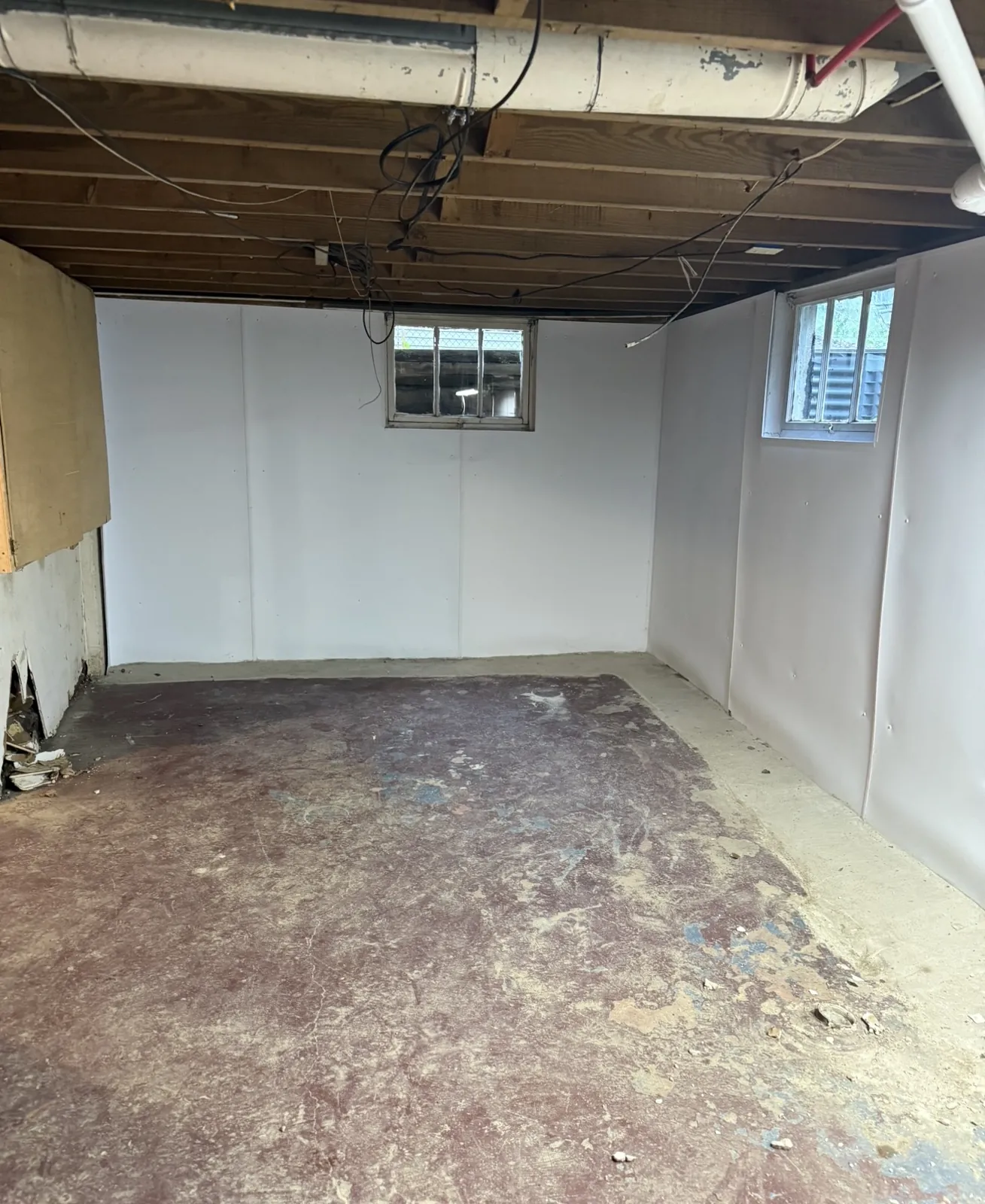 Basement room with white wall panels installed around two window wells above a bare concrete floor