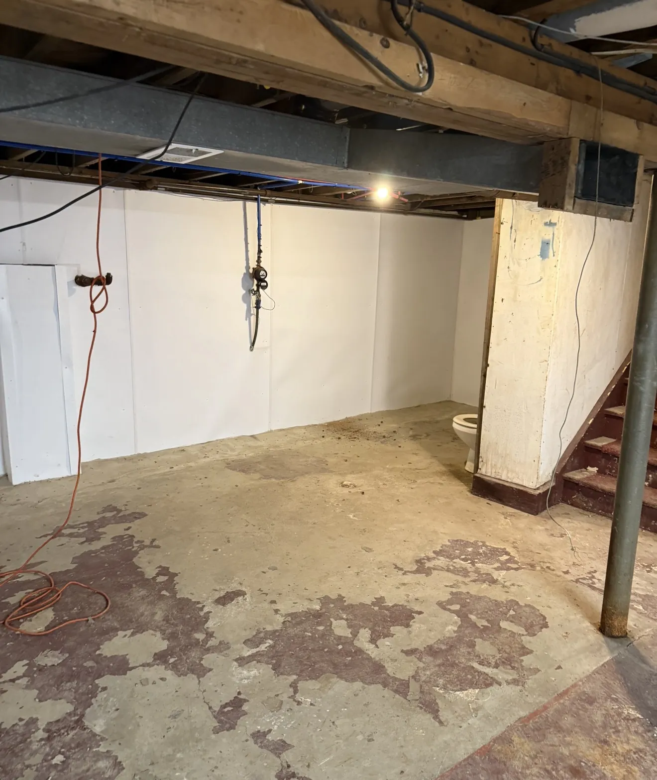 Basement with white wall panels behind the water meter and exposed floor area near the stairs