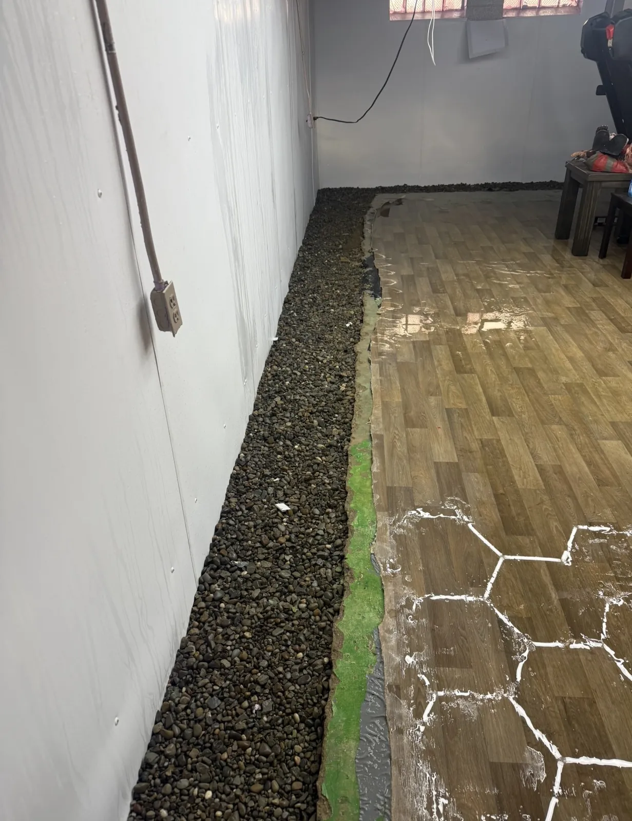Open perimeter drainage trench filled with gravel along a finished basement wall next to the floor