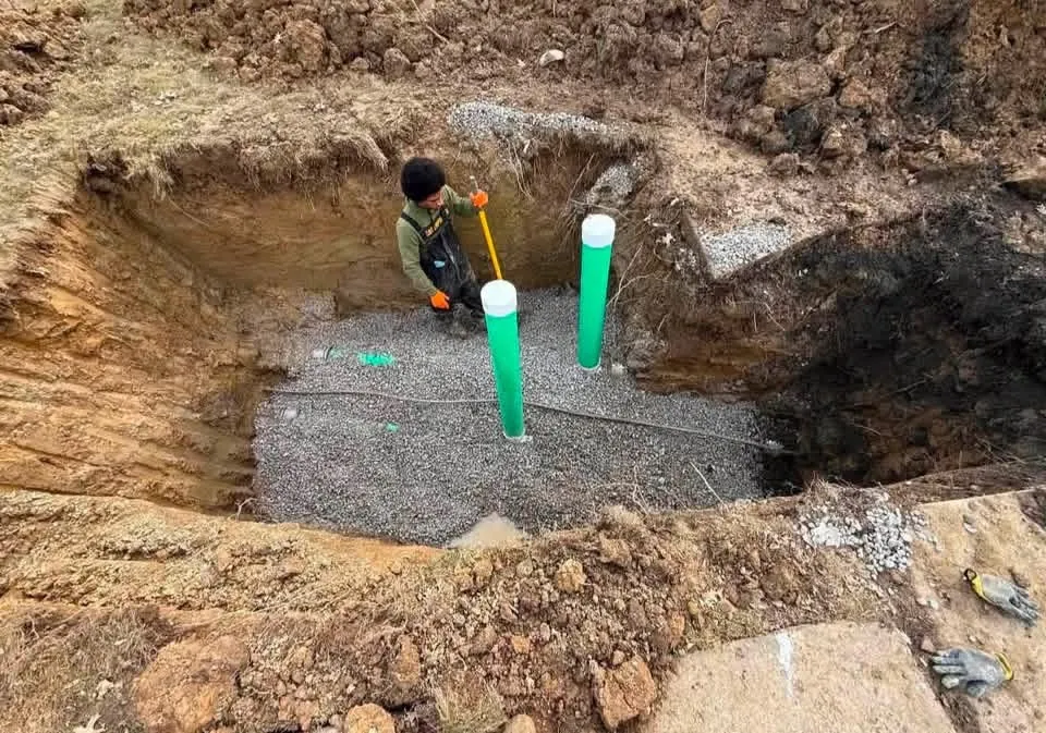 Worker leveling gravel around newly installed green sewer pipes in an excavation