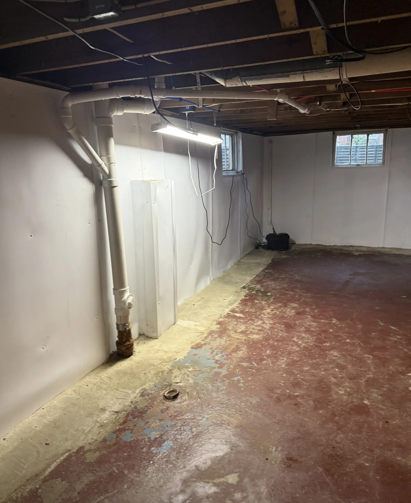 Basement corner with white wall liner and a restored concrete floor edge beside the drain piping