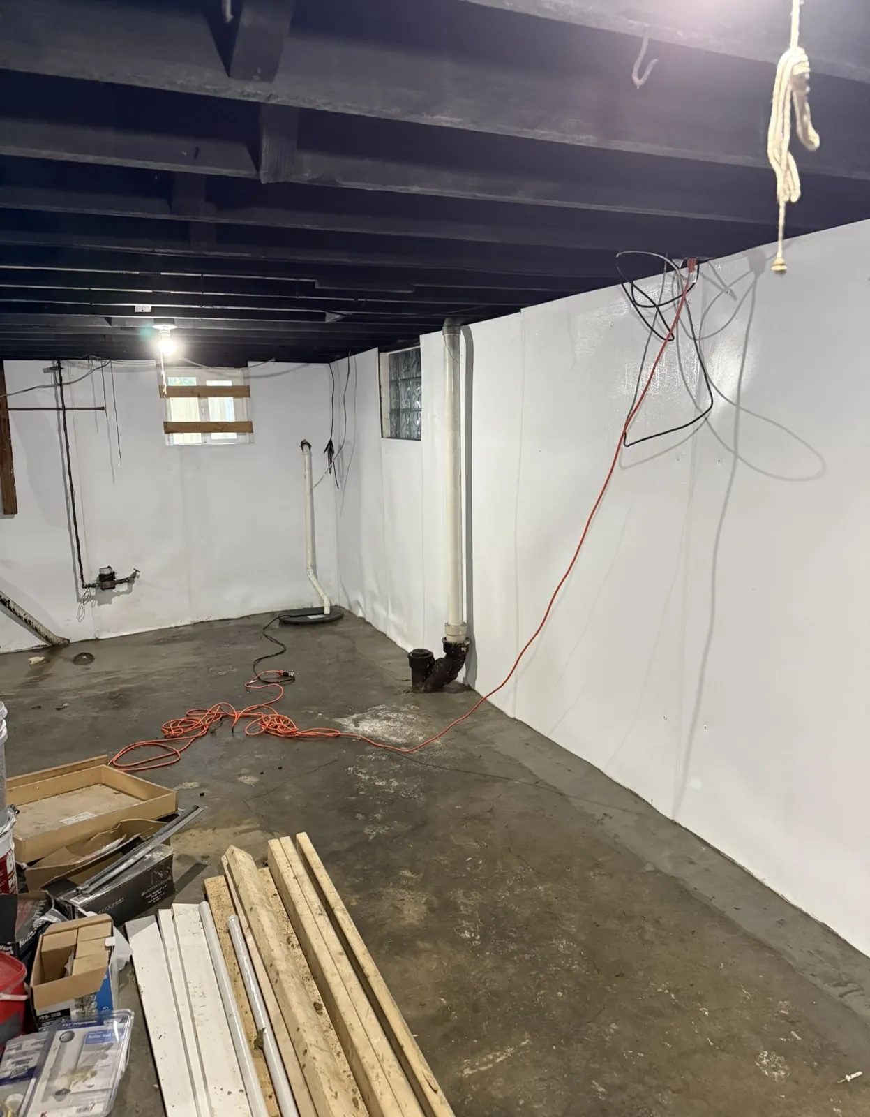 Basement with white wall liner along the perimeter, drain piping at the wall base, and a concrete floor