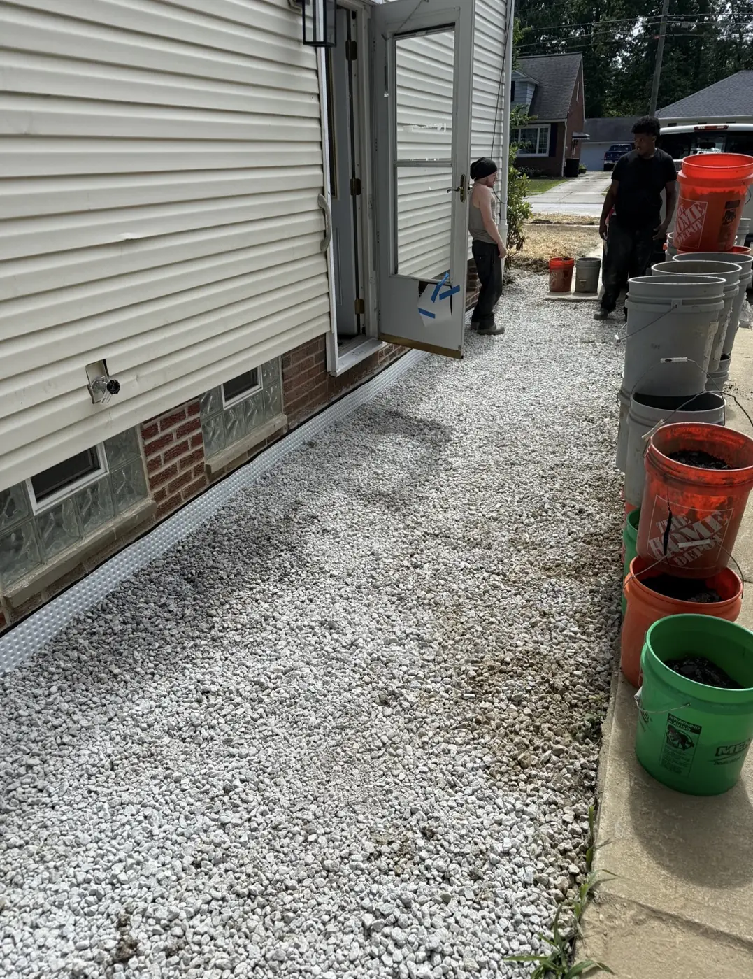 Foundation trench backfilled with white gravel with dimpled drainage membrane visible along the base of the house wall