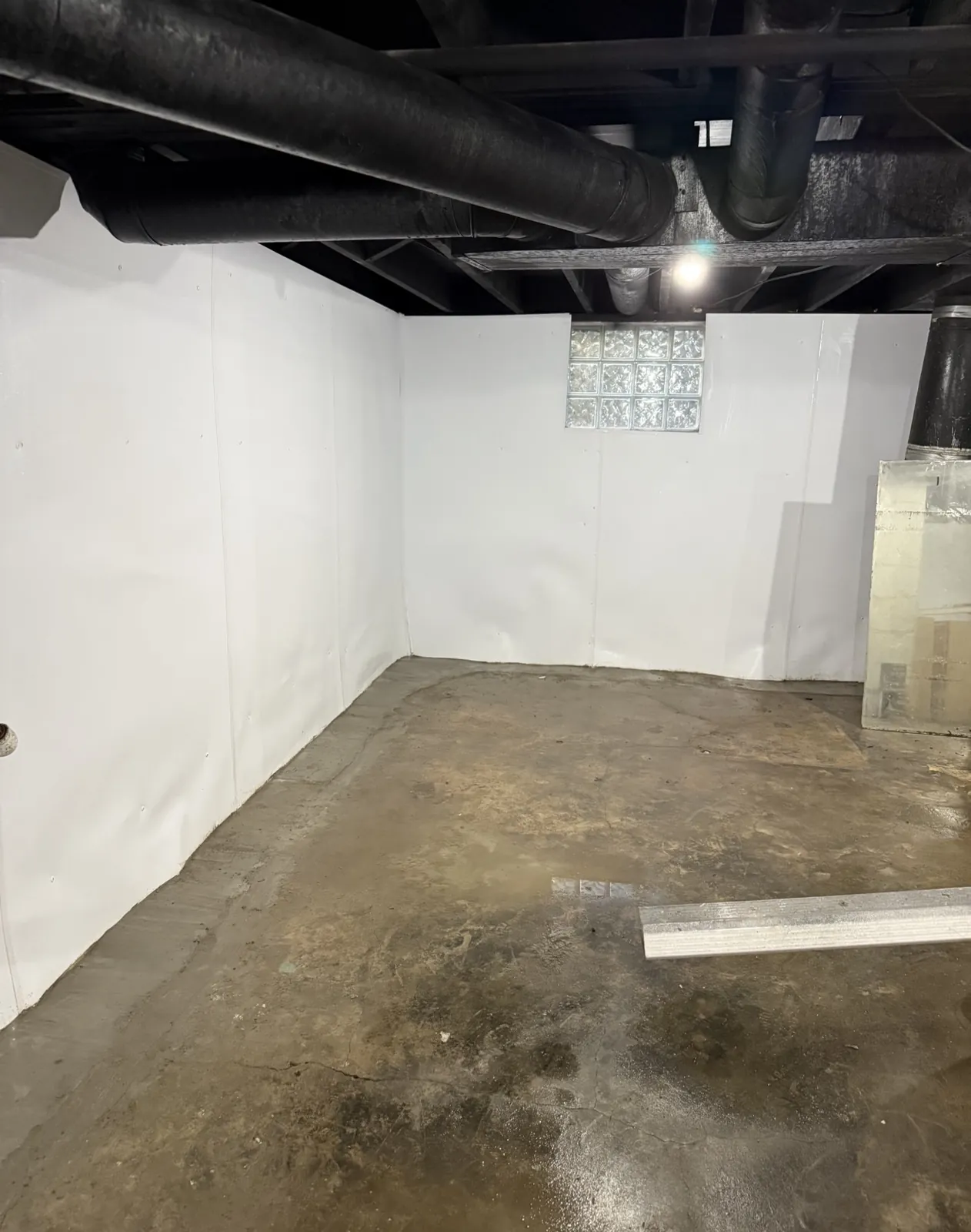 Basement walls lined in white panels with a clean concrete floor beneath overhead ductwork