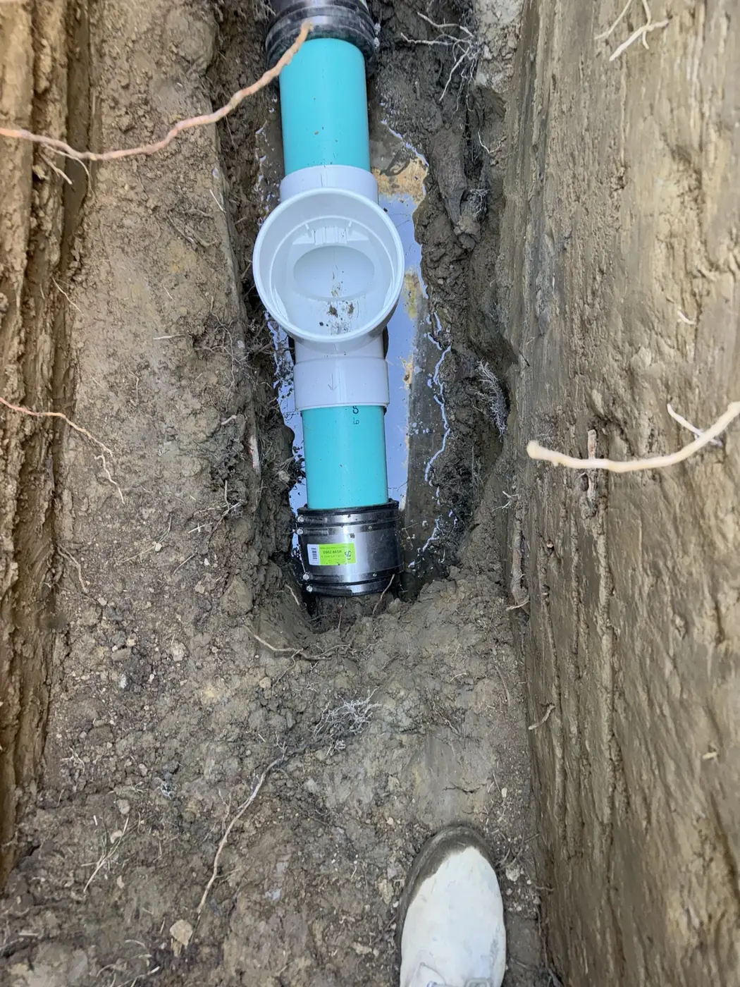 Backflow valve and cleanout fitting installed on a sewer main inside an excavated trench