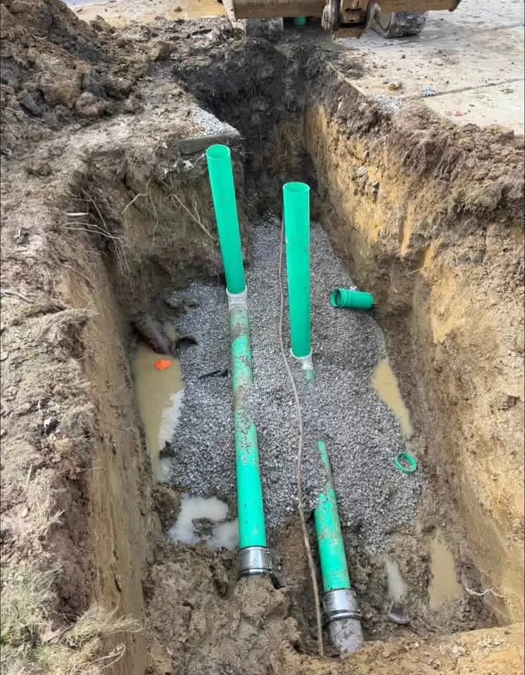 New green sewer pipe sections installed on a gravel base inside an excavated trench