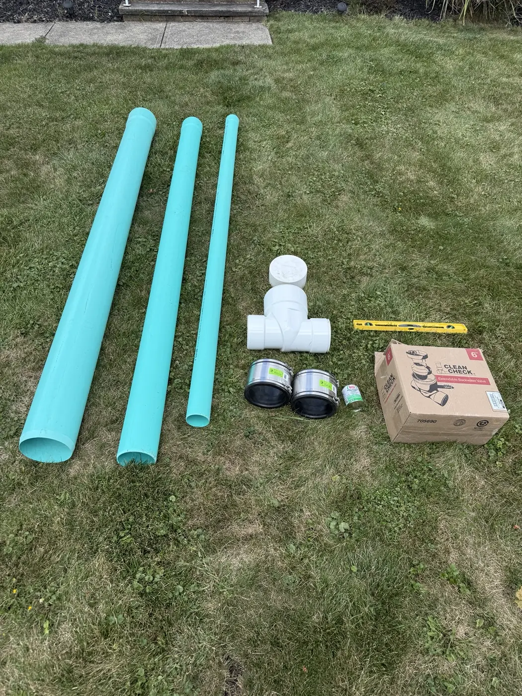 Sewer pipe, backflow valve, cleanout fittings, couplings, and installation materials laid out on grass